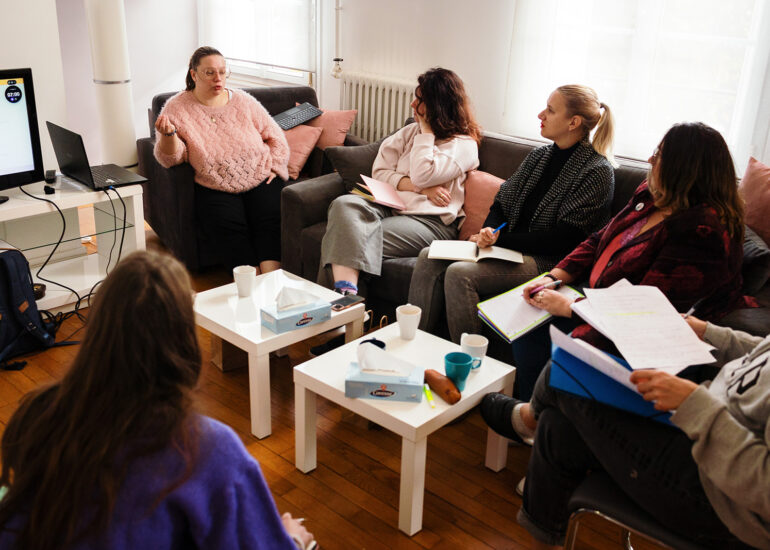 Groupe de photographes en discussion pendant un atelier photo-thérapie, carnets et cafés à la main.