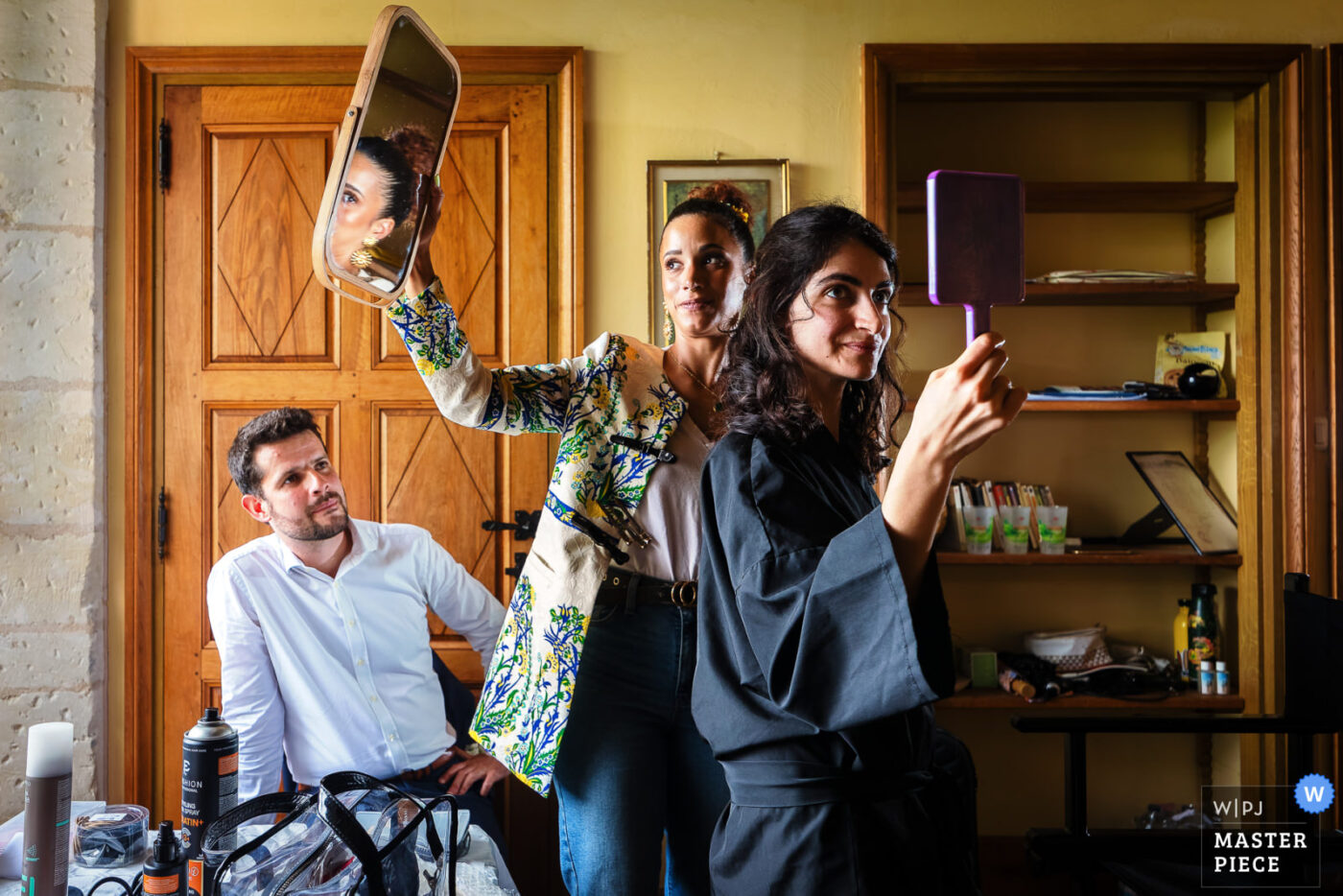 Mariée et proches se regardant dans des miroirs pendant les préparatifs avec un homme assis en arrière-plan