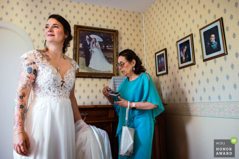 Mariée en préparation avec sa mère tandis que des photos d’elle et de son frère apparaissent en arrière-plan dans une chambre en Charente